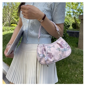Detail of floral embroidery and ruching on a light purple handbag with metal chain
