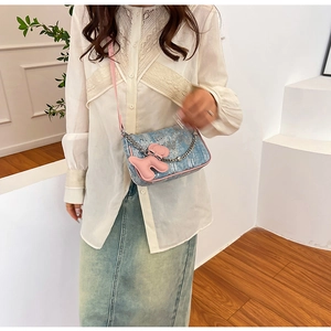 Detail of blue denim shoulder bag with pink trim and cute puppy charm on model