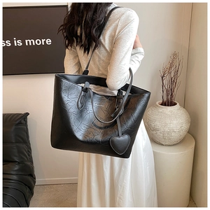 Nahaufnahme der schwarzen Tote-Tasche mit Lederfalten und Herzanhänger am Modell