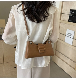 Detail of brown crocodile pattern baguette bag with a square buckle on a shoulder strap