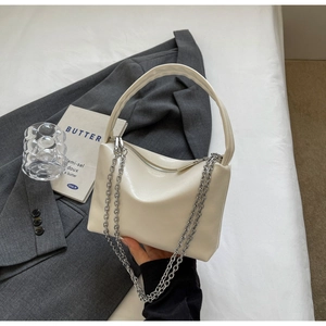 Detail of white patent leather handbag featuring a silver metal chain and smooth finish