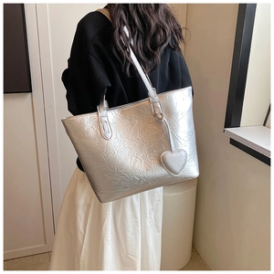 Detail der silbernen Metallic-Tasche mit Faltenstruktur und Herzanhänger am Modell