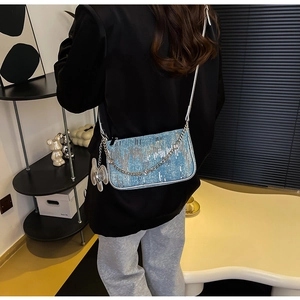 Detail of blue denim crossbody bag featuring silver sequins and a butterfly metal charm