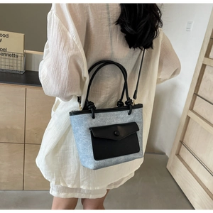 Détail du sac seau en denim bleu clair avec poche en cuir noir et poignée ronde