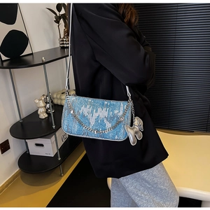 Detail of bright blue sequin shoulder bag with silver chain and dog charm on a model