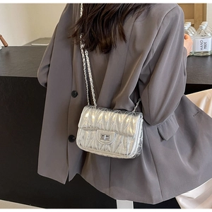 Sac bandoulière argenté matelassé porté par un mannequin sur un blazer gris