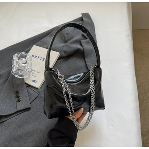 Detail of black glossy leather handbag featuring a stylish chunky silver metal chain