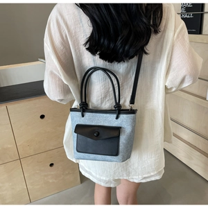 Détail du sac seau bleu-gris porté à l'épaule avec poignée ronde noire et bandoulière