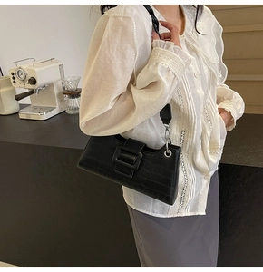 Detail of black crocodile texture baguette bag with buckle and woven strap
