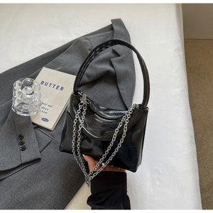 Detail of black patent leather handbag featuring glossy finish and silver chain decor