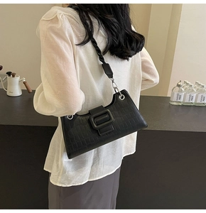 Detail of black crocodile texture baguette bag with wide buckle and braided shoulder strap
