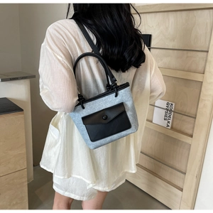 Détail du tissu denim bleu clair avec sangles en cuir noir sur le sac seau