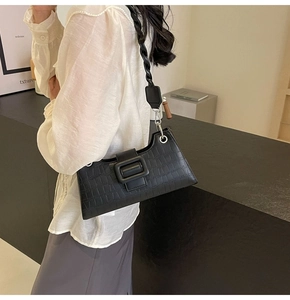 Detail of black faux leather underarm bag with crocodile pattern and woven strap design