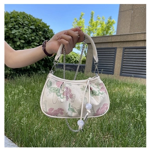 Close-up of vintage floral embroidery and metal chain on cream crossbody bag