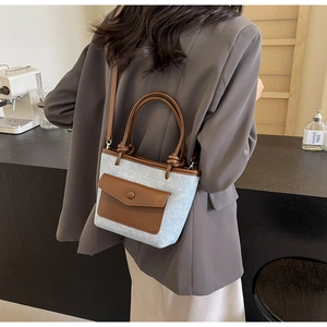 Détail du sac seau en denim bleu clair avec poignées en cuir marron porté par un modèle