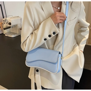 Detail der hellblauen Umhängetasche mit weißer Paspelierung über einem beigen Blazer