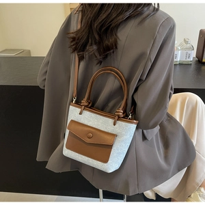 Détail du sac seau en denim bleu clair avec accents en cuir marron sur blazer gris
