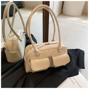 Detail of a beige glossy shoulder bag with twin front pockets and silver zipper on dark fabric
