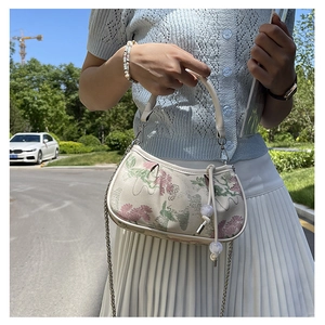 Detail of floral embroidery on cream crossbody bag with elegant bead pendant and chain