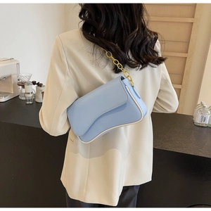 Detail der hellblauen Achseltasche mit asymmetrischer Klappe und goldener Kette am Modell