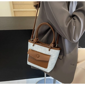 Détail du sac seau en denim bleu avec accents en cuir marron et bandoulière élégante