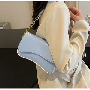 Detail der hellblauen Unterarmtasche mit Kontrastpaspeln und Goldkette an einem Model