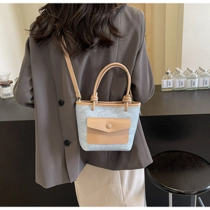 Détail d'un sac seau en denim bleu et cuir marron porté en bandoulière pour femme