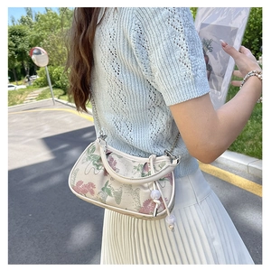Detail of floral embroidery on small square bag with pearl chain and leather handle