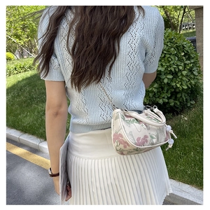 Detail of floral embroidery on a white crossbody bag with pearl charms and chain strap