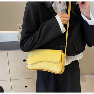 Detail einer glänzend gelben Ledertasche mit asymmetrischem Wellen-Design auf der Klappe