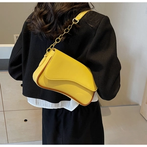Nahaufnahme einer hellgelben Satteltasche mit goldener Kette an einem Model