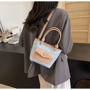 Détail du sac seau en denim bleu avec anses en cuir marron et poche avant à rabat boutonné