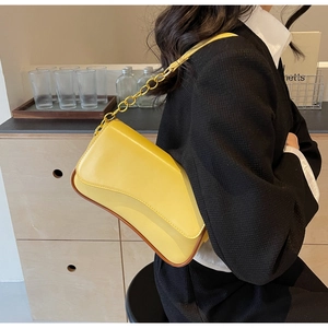 Seitenansicht einer gelben Umhängetasche mit Goldkette auf einem schwarzen Outfit