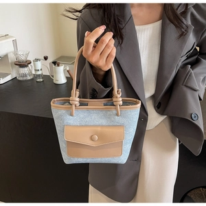 Détail du sac seau en denim avec bordure en cuir marron et sangle nouée tenue par modèle
