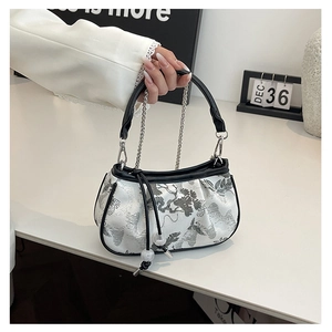 Close-up of white crossbody bag with silver embroidery, black leather handles and chain