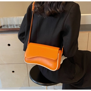 Detail der leuchtend orangefarbenen Umhängetasche mit weißen Paspeln am schwarzen Blazer
