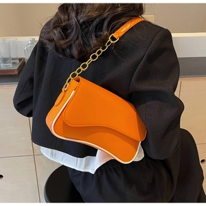 Detail der orangefarbenen Umhängetasche mit goldener Kette und weißer Paspelierung