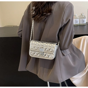 Close-up of silver quilted crossbody bag with chain strap and metal turn-lock on suit