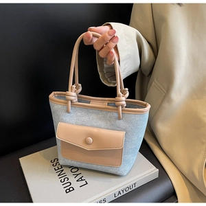 Détail du sac seau en denim bleu clair avec poignées en cuir marron et poche avant