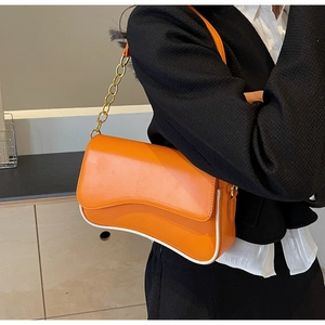Orangefarbene Umhängetasche mit weißen Paspeln und goldener Kette am Modell getragen