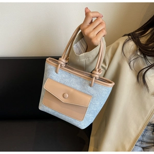 Détail d'un sac seau en denim bleu avec bordure en cuir kaki et poignée à nœud