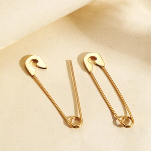 Vue détaillée de boucles d'oreilles épingles à nourrice dorées sur fond minimaliste
