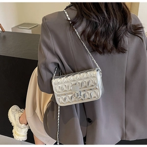 Detail of silver quilted chain bag with leaf-like texture on a grey suit model