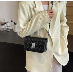Detail of a black quilted leather chain bag with a silver metal turn-lock on a model