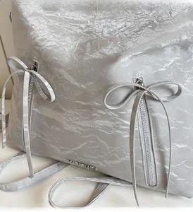 Detail of silver metallic wrinkled fabric bag with decorative bow and zippers