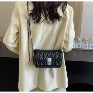 Detail of black quilted chain bag with silver rotating lock on a cream blazer