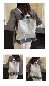 Detail of white textured backpack showing butterfly bow accents and metal zipper details