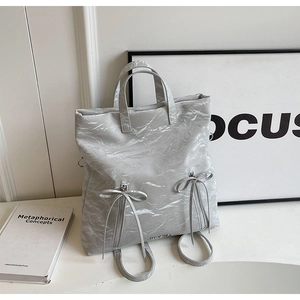 Detail of grey crinkled texture backpack with bow design and metallic zippers