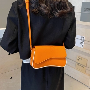 Orangefarbene Umhängetasche mit weißer Paspelierung und Wellenklappe am Model