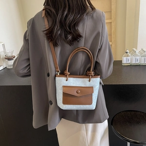 Sac seau chic en denim gris avec bordure en cuir marron porté par un mannequin
